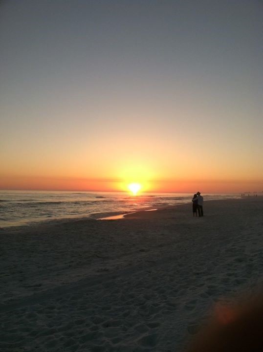 A group of people walking on a beach with a sunset in the background
Description automatically generated